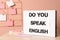 Stand with question Do You Speak English and stationery on table near pink wall