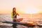 Stand up paddle boarding on a quiet sea with warm summer sunset colors. Happy smiling girl on board at sunset