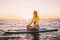 Stand up paddle boarding on a quiet sea with warm sunset colors. Young slim girl is relaxing on ocean