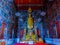 Standing golden Buddha statue in the temple with mural painting.