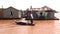 Standing man rows small boat on muddy Mekong river