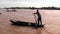 Standing man rows small boat on muddy Mekong river