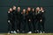 Standing and posing. Group of sportive women is outdoors near black building