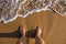 Standing on the shoreline while spuming sea water is surging towards brown sand at sunset