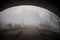 Standing under dark arched old bridge on creepy eerie footpath with fog and mist surrounding. Spooky atmosphere all alone.