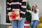 Standing woman hiding golden gift box behind her back from girl friend in christmas party