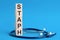 Staph word written on wooden blocks and stethoscope on light blue background