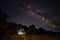 The starry sky and the Milky Way over a small simple house in the forest. Night photo.