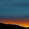 Stars in night sky at dusk. Horizon line, mountains, sun light just behind the horizon, orange blue colored light sky with the