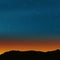 Stars in night sky at dusk. Horizon line, mountains, sun light just behind the horizon, orange blue colored light sky with the