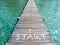 Start, white text and arrow on wooden bridge heading to the sea. Wood plank pathway bridge on clear sea water at the port in.