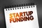 Startup Funding - act of raising capital to support a business venture, text concept on notepad