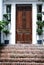 Stately wooden door with topiary on each side and brick stairs in Charleston, South Carolina.