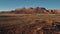 Static drone shot of American canyon mountain ridge panorama, car taking off small parking in the middle of the desert.