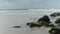 Static shot of ocean waves washing over sea rocks with a big sky in the background