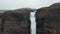 Static shot of to part of tall waterfall. Mass of white water rolling over rounded edge of tall rocky cliff and falling
