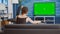 Static tripod shot of young woman watching movie on tv with green screen and eating popcorn
