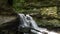 Stationary view of waterfall pouring through canyon in forest