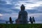 Statue of Buddha and three young women watching sunset over Pacific ocean