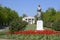 Statue of a collective farmer on a pedestal. The legacy of the Soviet era. A flower bed with tulips and young trees in