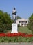 Statue of a collective farmer on a pedestal. The legacy of the Soviet era. A flower bed with tulips and young trees in