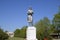 Statue of a collective farmer on a pedestal. The legacy of the Soviet era. A flower bed with tulips and young trees in