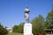 Statue of a collective farmer on a pedestal. The legacy of the Soviet era. A flower bed with tulips and young trees in