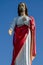 statue in color of Jesus to his full height on blue background of clear sky on a sunny day. Jesus stands holding his left hand on