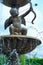 The statue of the Cupid in the cement fountain at the outdoor park with defocused water drop in foreground