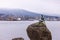 A statue of a girl in a swimsuit on a boulder on a shore of Vancouver Harbor