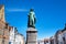 Statue of Jan Van Eyck and medieval house exterior against blue sky in Brugge, Belguim