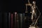 Statue of Lady Justice near books on dark background, space for text. Symbol of fair treatment under law