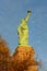The Statue of Liberty seen from the side with warm afternoon sun, fall trees and blue cloudy sky