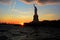 Statue of Liberty in silhouette at sunset viewed from the water with clouds and colorful sky