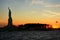 Statue of Liberty in silhouette at sunset viewed from the water with Flag, clouds and colorful sky