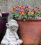 Statue of monkey sitting next to terracotta flower pot full of colourful pansies in a suburban garden.