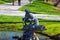 A statue of two boys sitting on a tree in a lake surrounded by silky green lake water, lush green grass, people walking