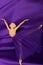 The statuette of a ballerina in a skirt lies on a glossy fabric of lilac color