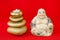 Statuette of a laughing Buddha with stones and a candle, on a red background, Feng Shui.
