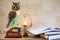 Statuette of an owl, a stack of books with an open book and a lit candle on a mantelpiece. Owl as a symbol of wisdom and knowledge