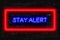 Stay Alert Neon sign on a dark brick background