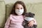 Stay at home in quarantine, funny kid with toy on couch during COVID-19 coronavirus pandemic. Little girl in medical mask for