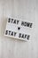 `Stay home stay safe` words on a lightbox on a white wooden surface, top view. Overhead, from above, flat lay