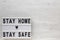`Stay home stay safe` words on a lightbox on a white wooden surface, top view. Overhead, from above, flat lay. Copy space
