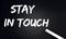 STAY IN TOUCH Text on Black Chalkboard with a piece of chalk