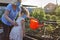 Staycation in summer cottage. Granny with girl in medical masks watering plants at backyard
