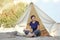 Staycations - local camping outdoor vacation. Woman drinking tea near big glamping tent with cozy interior. Luxury travel