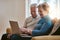 Staying tech savvy during the senior years. a happy senior couple using a laptop together on the sofa at home.