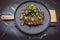 a steak on a black plate with salad on top on a marble surface