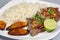 A steak covered in pico de gallo surrounded by plantains and white rice on a white plate. Cuban food.